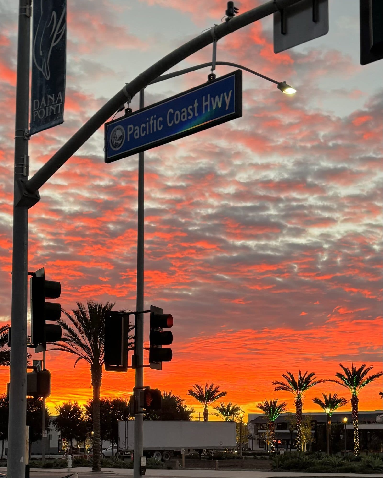 Red sunrise sky over Pacific Coast Highway, palms and signal lights in silhouette